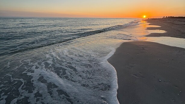 A beach at sunset with waves gently lapping onto the shore. - Sanddollar C101: Gorgeous Reno & Decor Gulf-Front! (Sanibel)