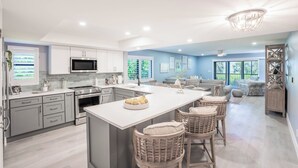 A modern kitchen with a central island, stainless steel appliances, and a dining area with wicker chairs. - Sanddollar C101: Gorgeous Reno & Decor Gulf-Front! (Sanibel)