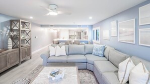 A modern living room with a sectional sofa, a coffee table, and a dining area in the background. - Sanddollar C101: Gorgeous Reno & Decor Gulf-Front! (Sanibel)