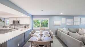 A modern kitchen with white cabinets, a central island, and a dining area with a table set for six. - Sanddollar C101: Gorgeous Reno & Decor Gulf-Front! (Sanibel)