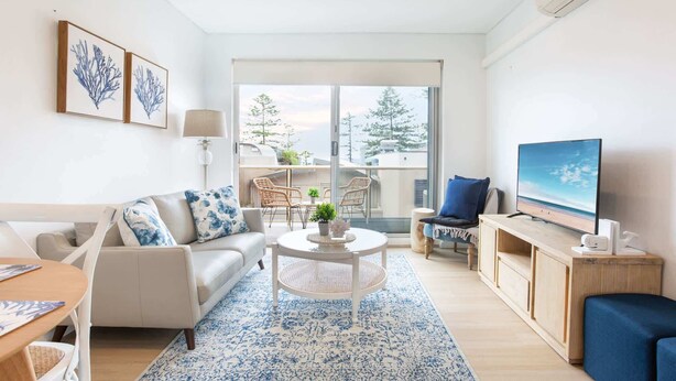 Una sala de estar moderna con un sofá, una mesa de centro, un televisor y un balcón con mobiliario exterior.