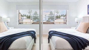 Habitación con espejos, dos camas, un ventanal y vistas a edificios y árboles.