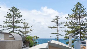 Una terraza en la azotea con vistas al mar, rodeada de pinos y arquitectura moderna.