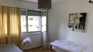 A room with a bed, a small table with a towel, a window with blinds, and a painting on the wall. - Bijou Apartment (Zollikofen)
