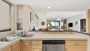 A modern kitchen with a dishwasher, double sink, and wooden cabinets. - Summer Deal Golfers Paradise Condo with Fairway and Ocean Views (Waikoloa)