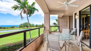 A balcony with a glass table and chairs, overlooking a golf course and ocean. - Summer Deal Golfers Paradise Condo with Fairway and Ocean Views (Waikoloa)