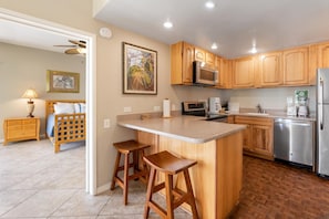 A kitchen with wooden cabinets, a central island with stools, a microwave, a refrigerator, and a dishwasher. - New Listing, Royal Sea Cliff 705, Ocean View, AC (Kailua Kona)