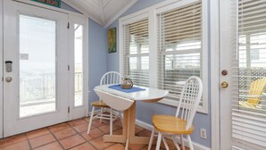 Una habitación con una puerta blanca que indica “DOLPHIN BLVD”, una pequeña mesa con sillas y una ventana con persianas.