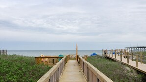 Pasarela de madera que lleva a una playa con una estructura de madera y una torre de salvavidas.