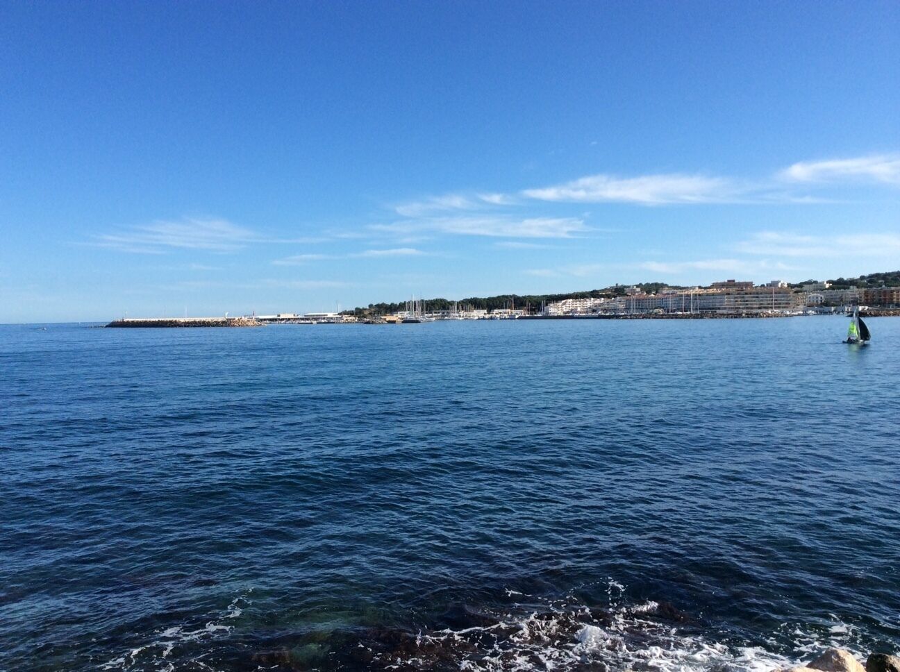 Eine Küstenansicht mit blauem Himmel, ruhiger See und einer entfernten Uferlinie mit Gebäuden.