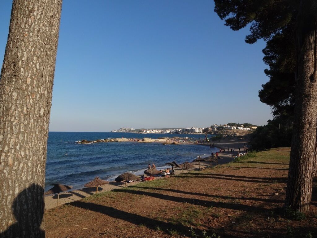 Vista costera con cielo despejado, playa de arena y algunas sombrillas.