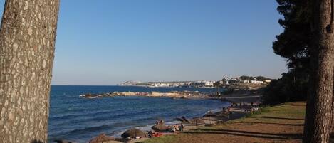 Vista costera con cielo despejado, playa de arena y algunas sombrillas.