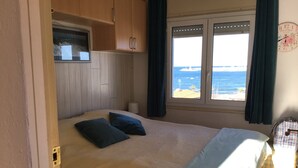 Ein Schlafzimmer mit Bett, einem Fenster mit Vorhängen, einer Wanduhr und Blick aufs Meer.