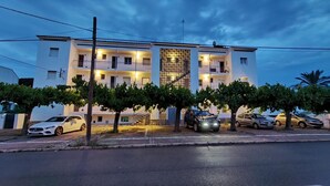 Ein mehrstöckiges Hotel mit Balkonen, einer zentralen Wandverzierungen und parkenden Autos davor.