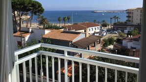Ein Küstenwohngebiet mit Häusern mit Terrakotta-Dächern, Blick auf das Meer und einer Promenade mit Palmen.