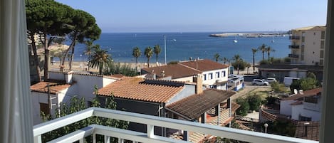 Un área residencial costera con casas de techo de teja anaranjada, vista al mar y un paseo marítimo con palmeras.