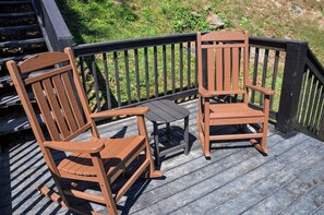 Una terraza de madera con dos mecedoras y una pequeña mesa.