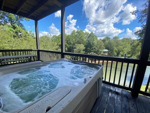 A hot tub on a wooden deck with a view of a lake and trees. - River Front Lodge • Close tot he Folk School • (Murphy)