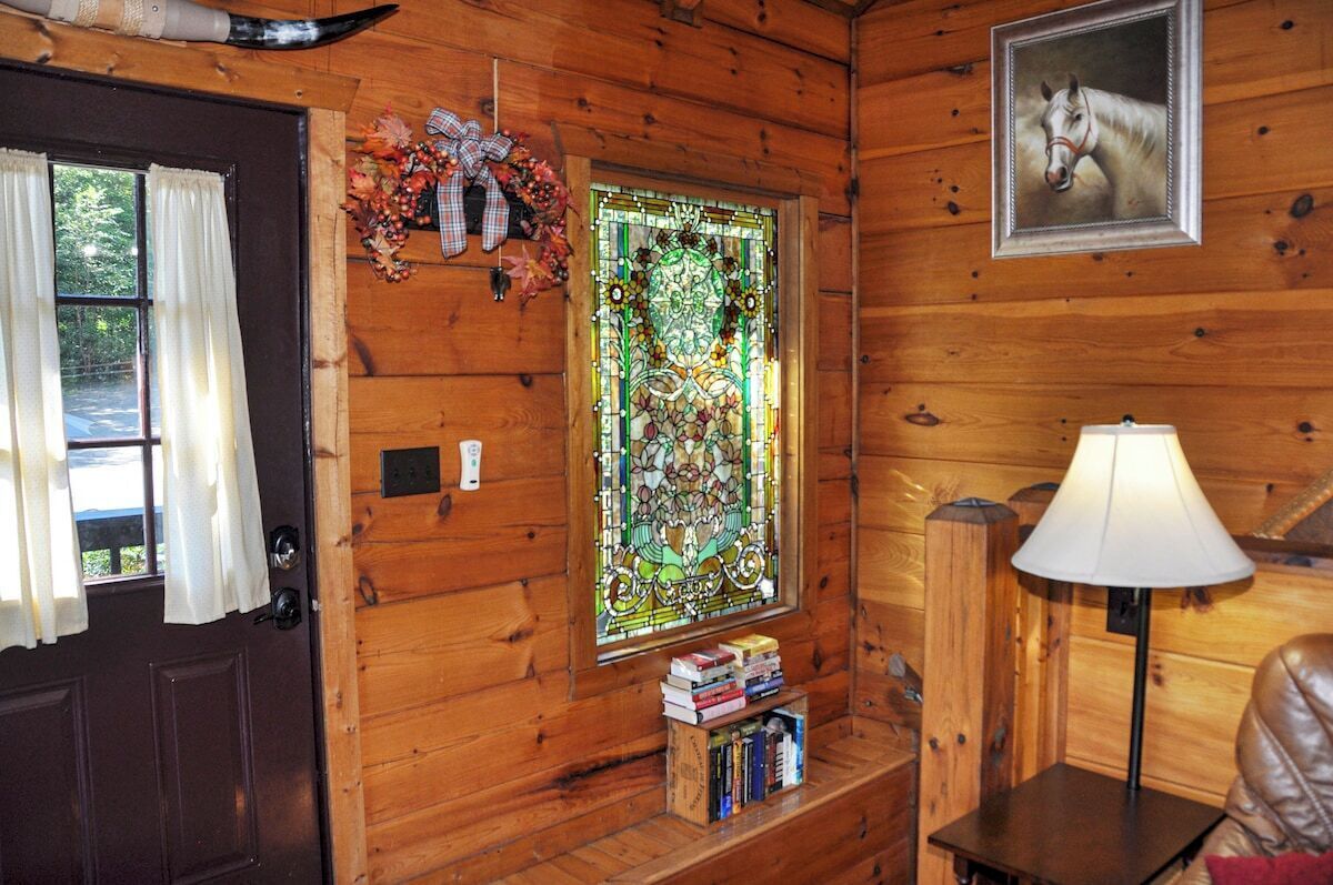 L’intérieur d’un chalet en bois, avec un vitrail, une porte ornée de rideaux, un tableau encadré représentant un cheval, une lampe et une petite bibliothèque.