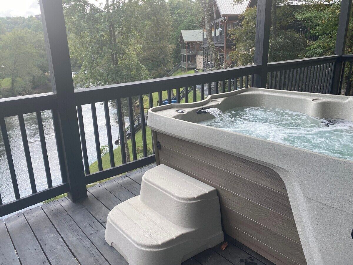 A hot tub on a wooden deck with a view of a lake and a building in the background.