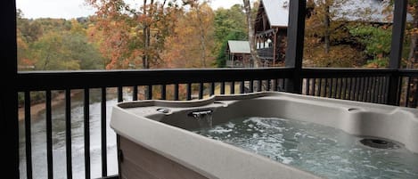 A hot tub on a wooden deck with a view of a river and autumn trees.