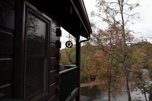 Una cabaña de madera con ventana y puerta, con vista a un río y follaje otoñal.