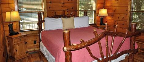 A wooden cabin bedroom with a four-poster bed, two bedside lamps, a wooden nightstand, and a window with blinds.