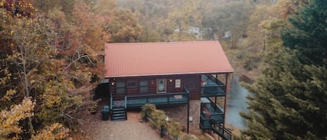 A cabin with a red roof, surrounded by trees and a body of water.