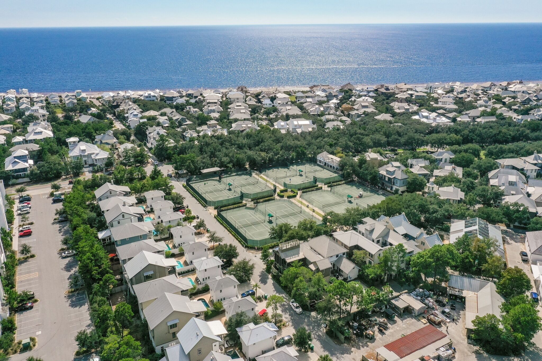 Vista aérea de una zona residencial con casas, una cancha de tenis y una playa al fondo.