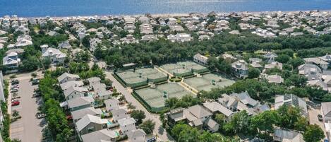 Vista aérea de una zona residencial con casas, una cancha de tenis y una playa al fondo.