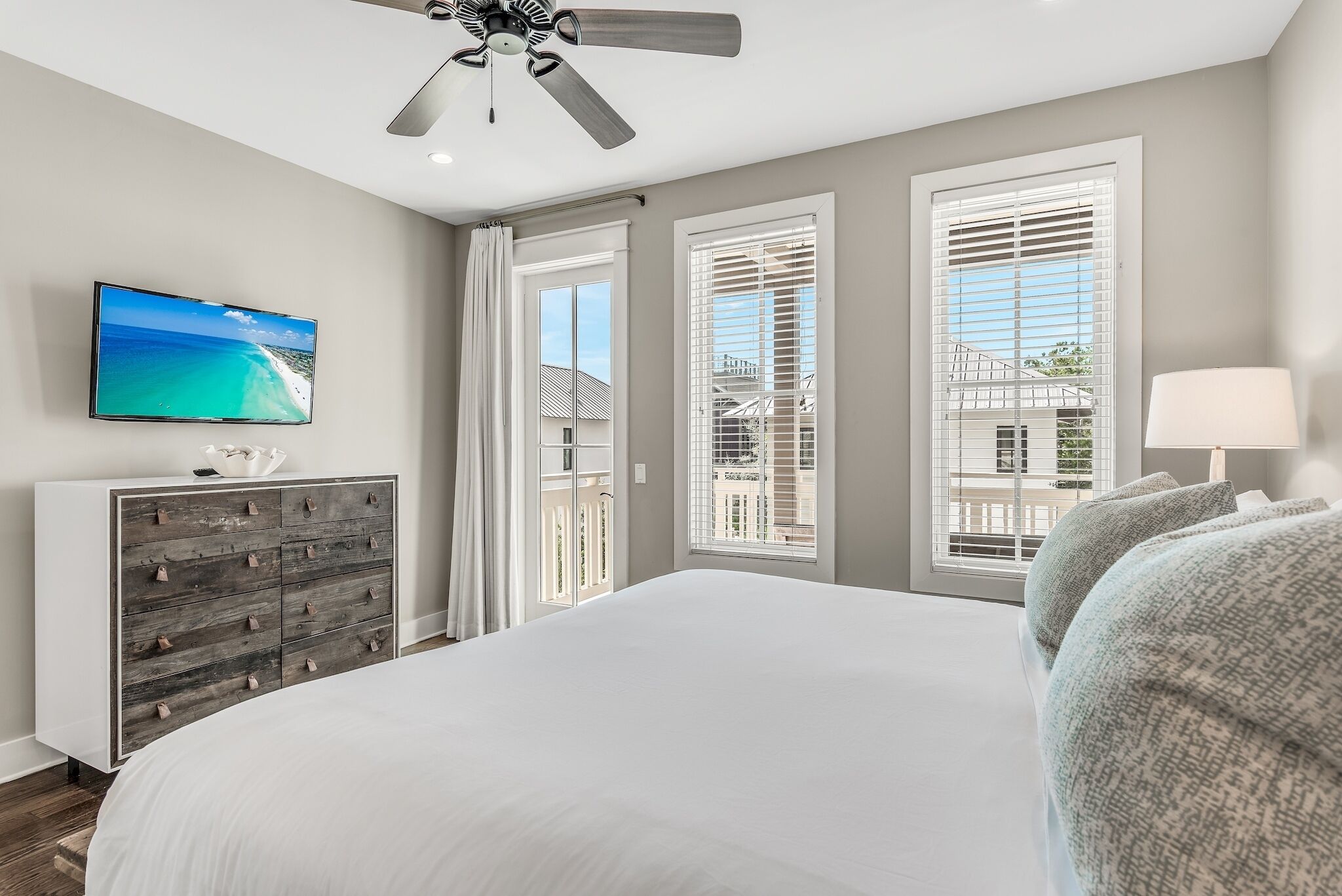 A bedroom with a large bed, a ceiling fan, a TV on the wall, and a dresser.
