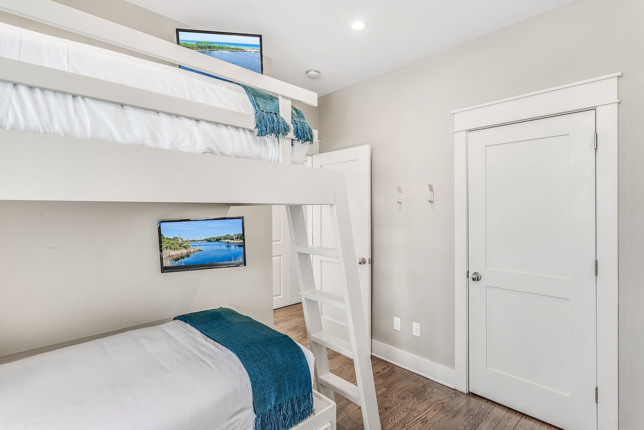 A room with a bunk bed, a desk with a computer, a door, and a wall-mounted TV.
