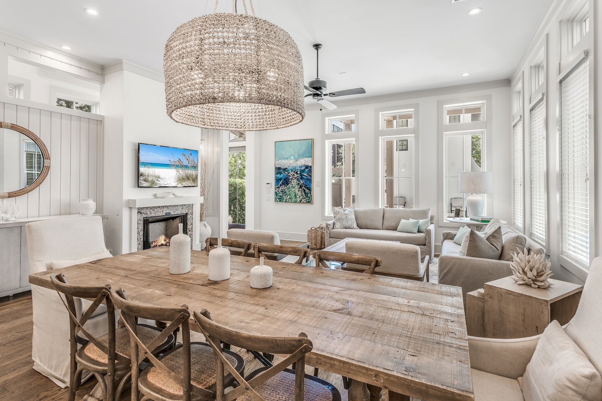 A spacious living room with a large wooden dining table, comfortable seating, a fireplace, and large windows.
