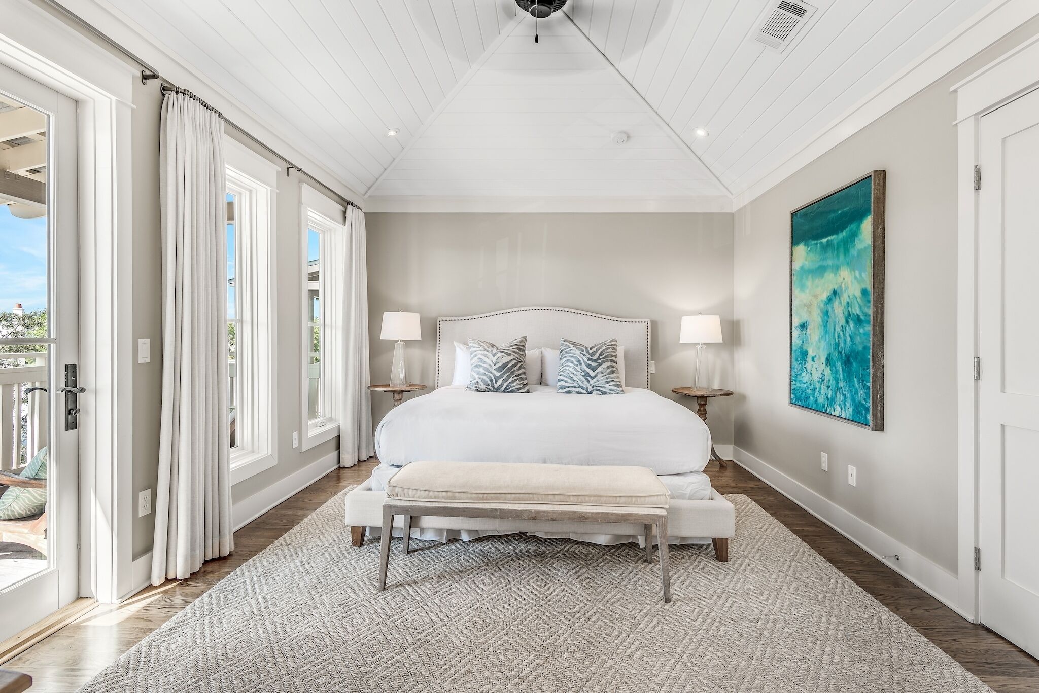 A spacious bedroom with a large bed, a bench, and a view of the outdoors through a sliding door.