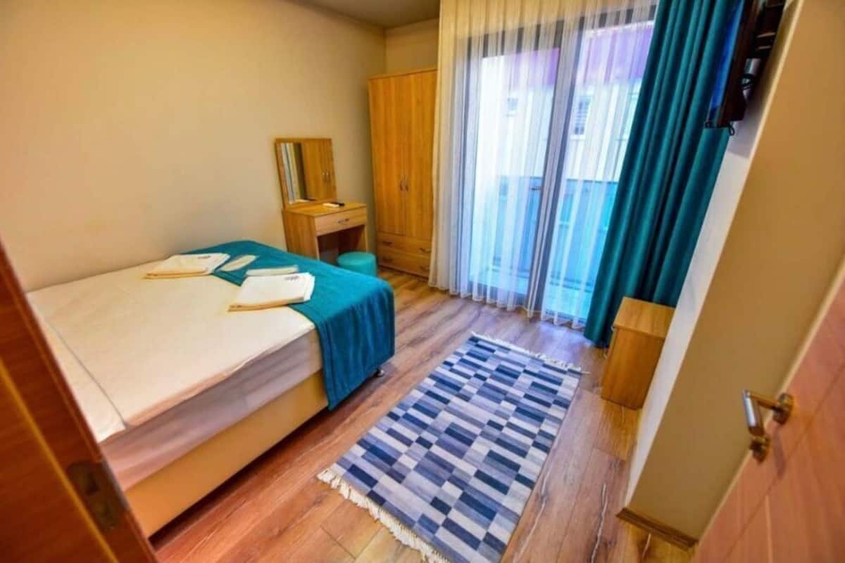 A small bedroom with a bed, a desk, a wardrobe, and a window with curtains.
