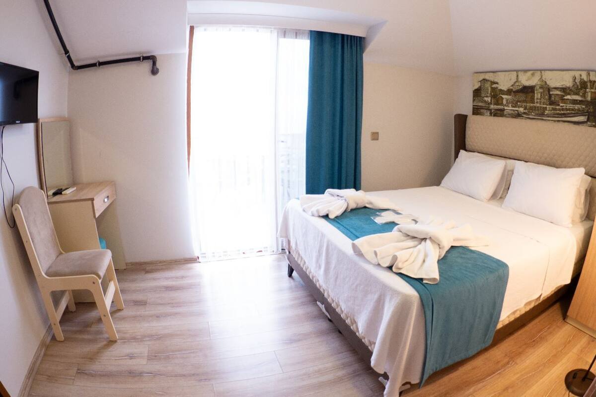 A hotel room with a bed, a desk, a chair, a TV, and a painting on the wall.