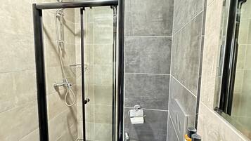 Un baño moderno con ducha envuelta en vidrio, bañera blanca y tocador con artículos de aseo.