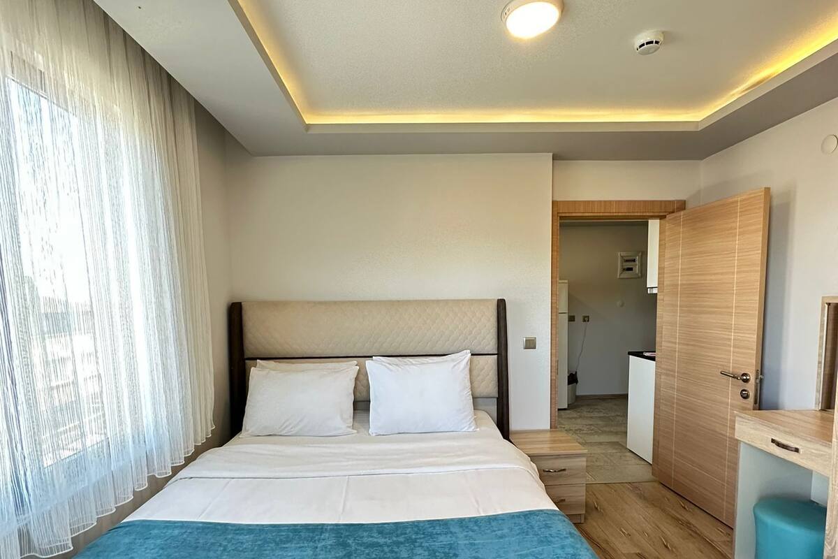 A modern hotel room with a large bed, a bedside table, a wardrobe, and a bathroom visible through an open door.