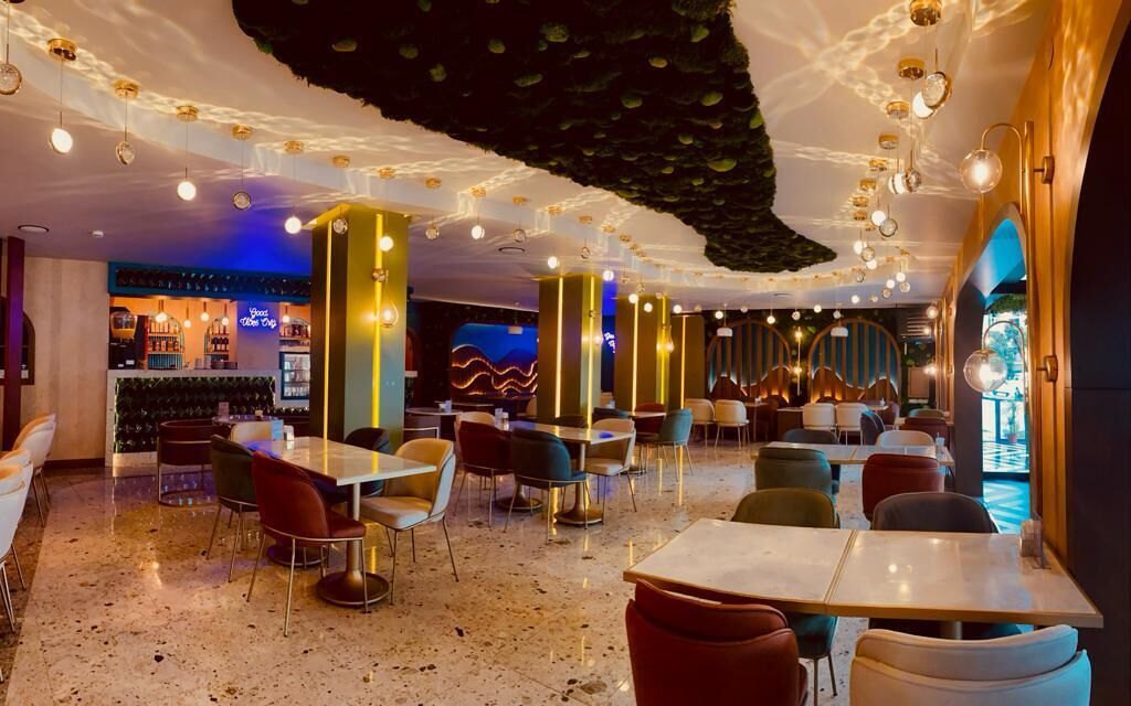 Interior moderno de restaurante con mesas y sillas, una zona de bar e iluminación decorativa.