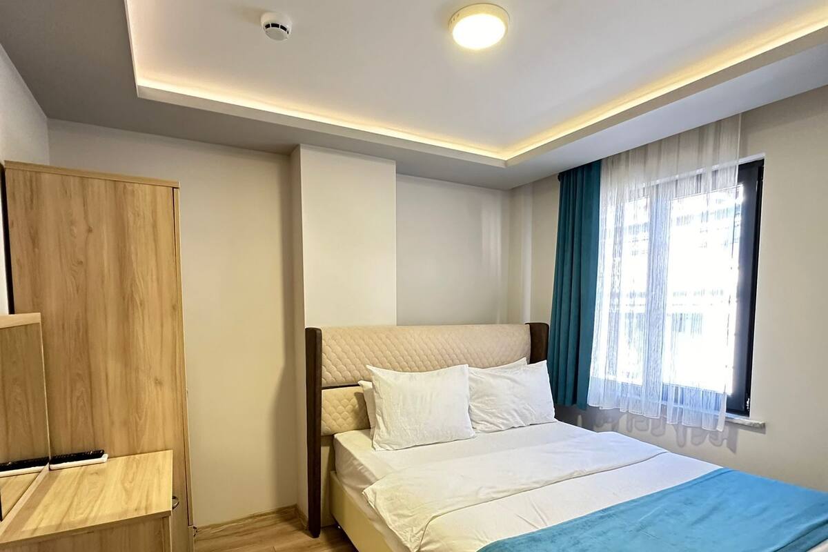 A bedroom with a bed, a wardrobe, a window with curtains, and a ceiling light.