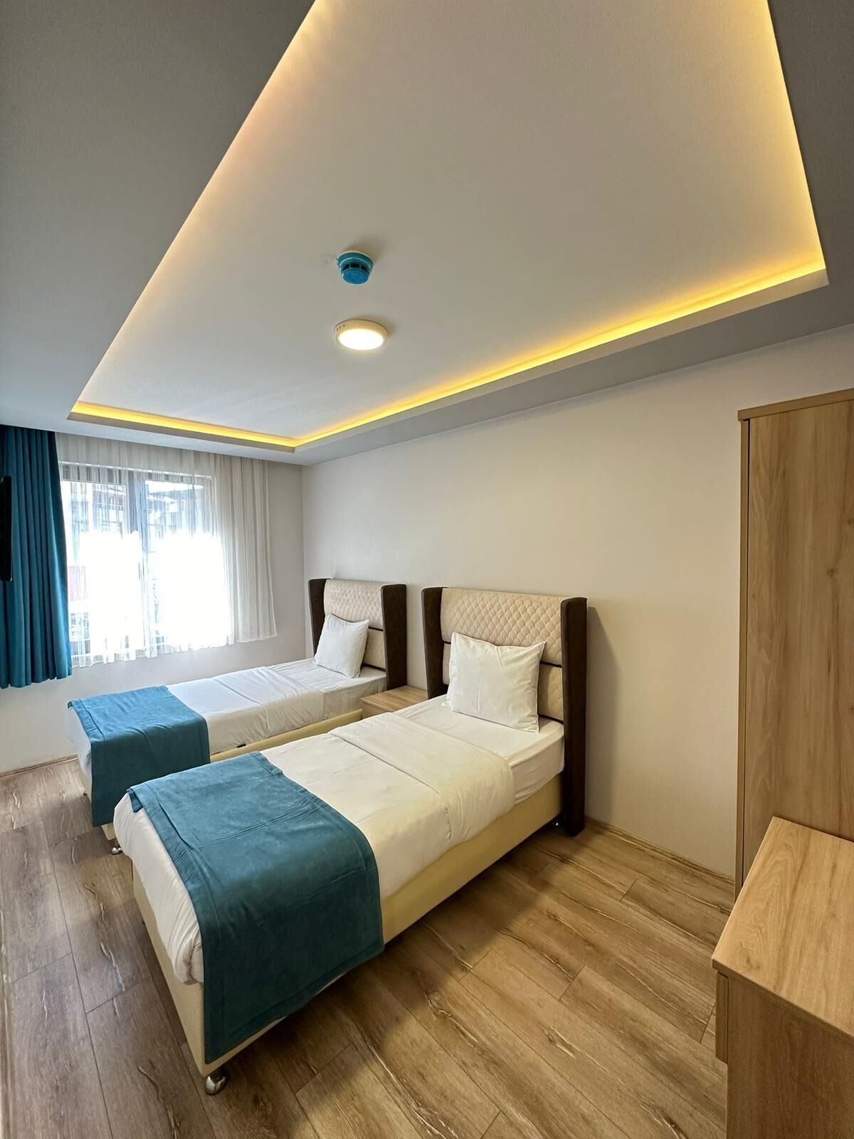 A hotel room with two beds, a wooden wardrobe, and a ceiling light.