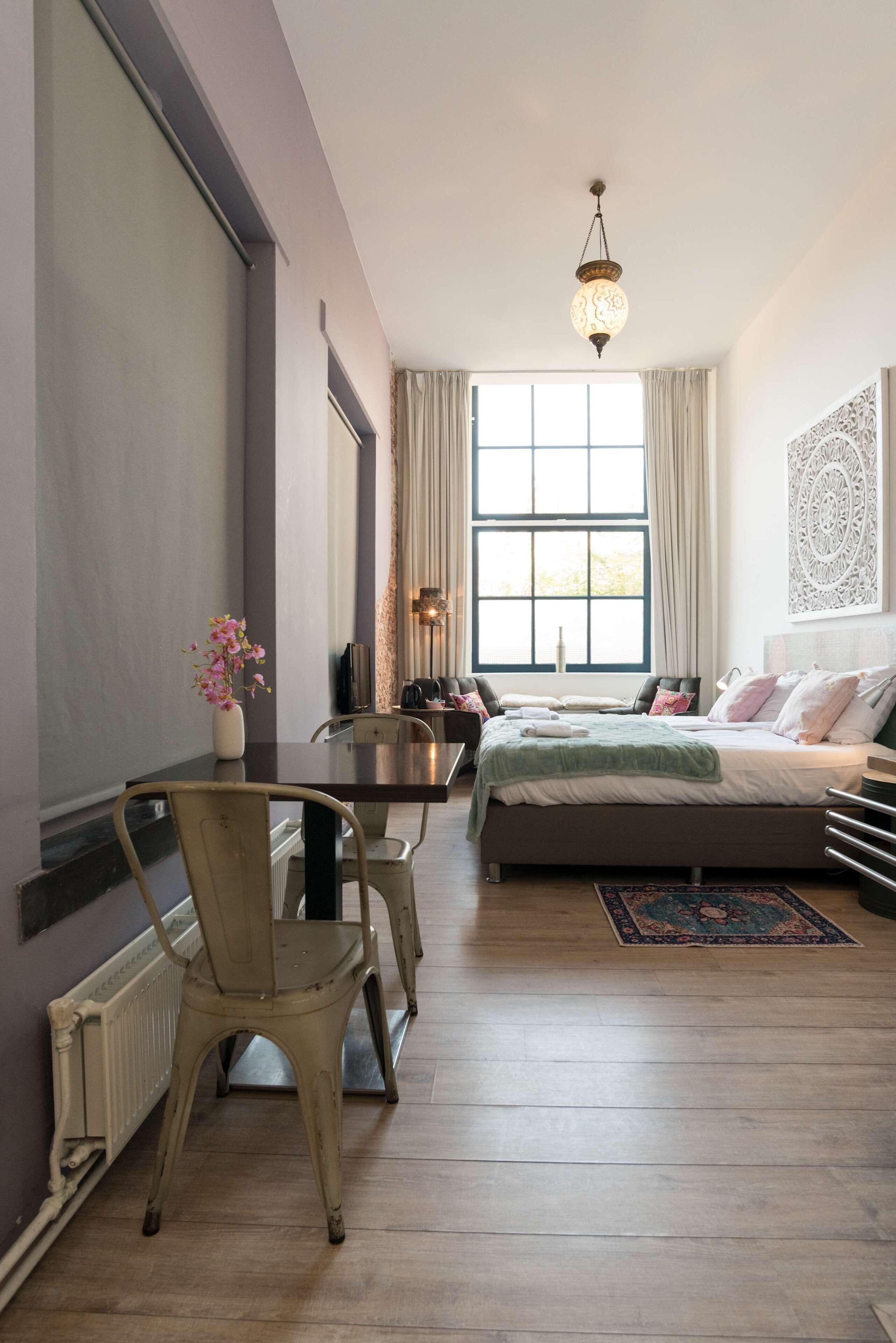 A bedroom with a bed, a table, chairs, a window, and a decorative wall piece.