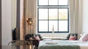 Een slaapkamer met een bed, een bureau, een stoel, een lamp en een raam met gordijnen.