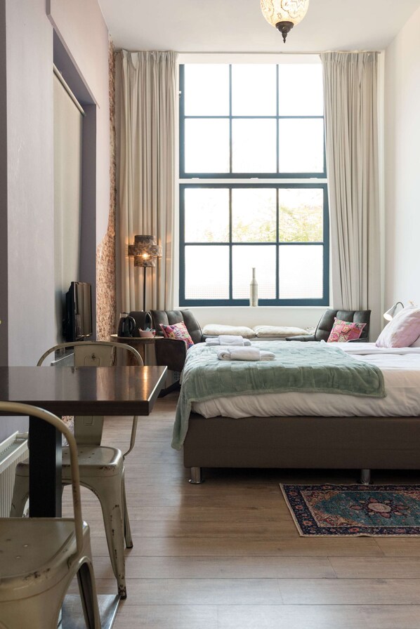 A bedroom with a bed, a desk, a chair, a lamp, and a window with curtains.