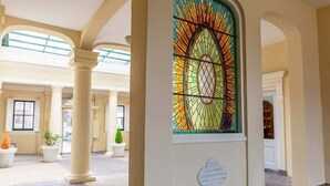 Een hotel lobby met een groot glas-in-lood raam, zuilen en plantenpotten.