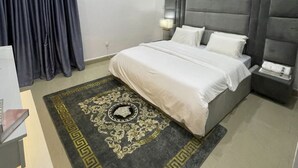 A modern hotel room with a large bed, grey padded headboard, and a decorative rug. - Lovely luxury 3 bedroom apartment (Lagos)