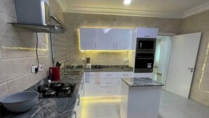 A modern kitchen with white cabinets, a built-in oven, and a central island. - Lovely luxury 3 bedroom apartment (Lagos)