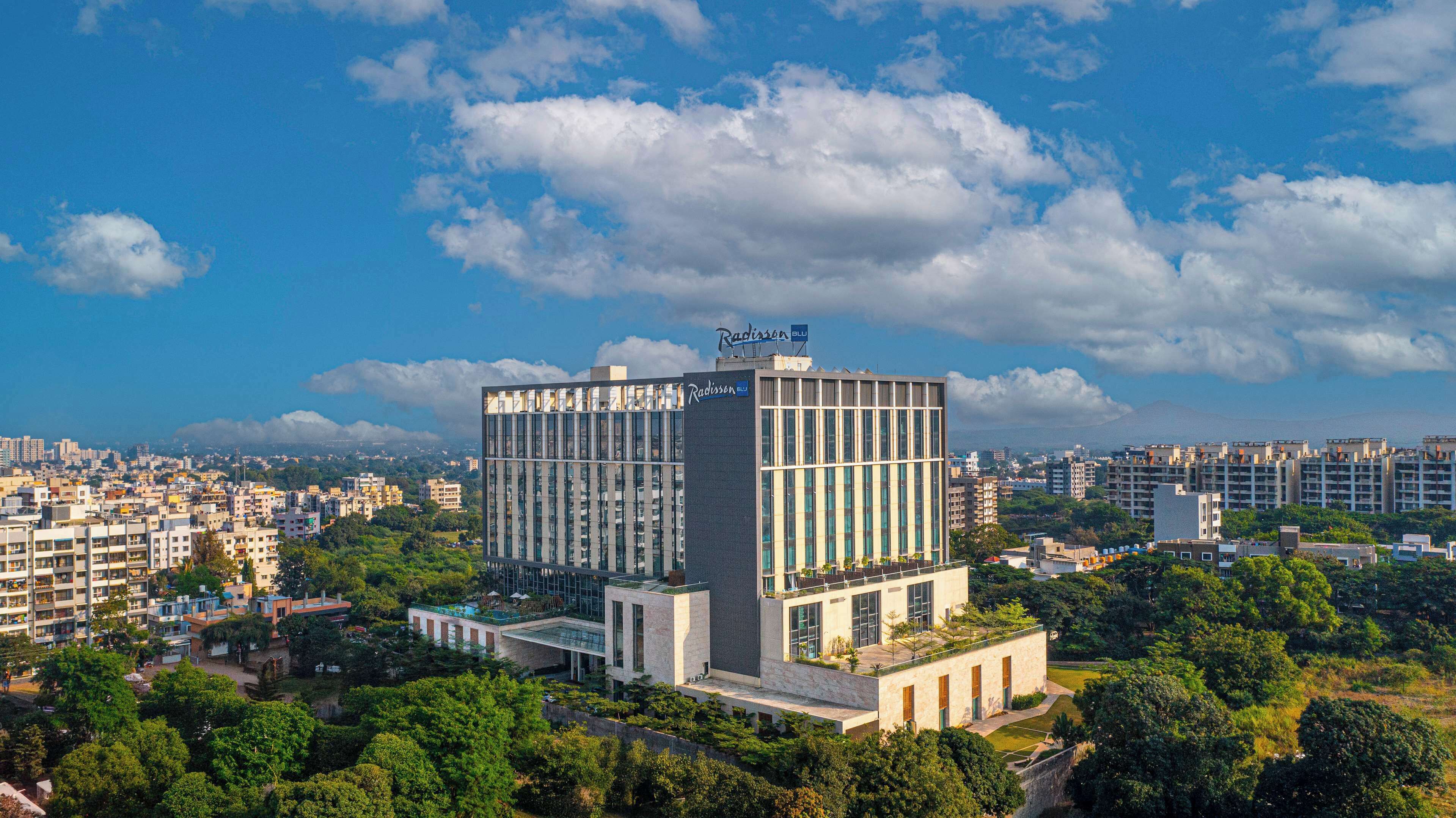 A modern Radisson Blu hotel with a prominent glass facade, surrounded by urban buildings and greenery.