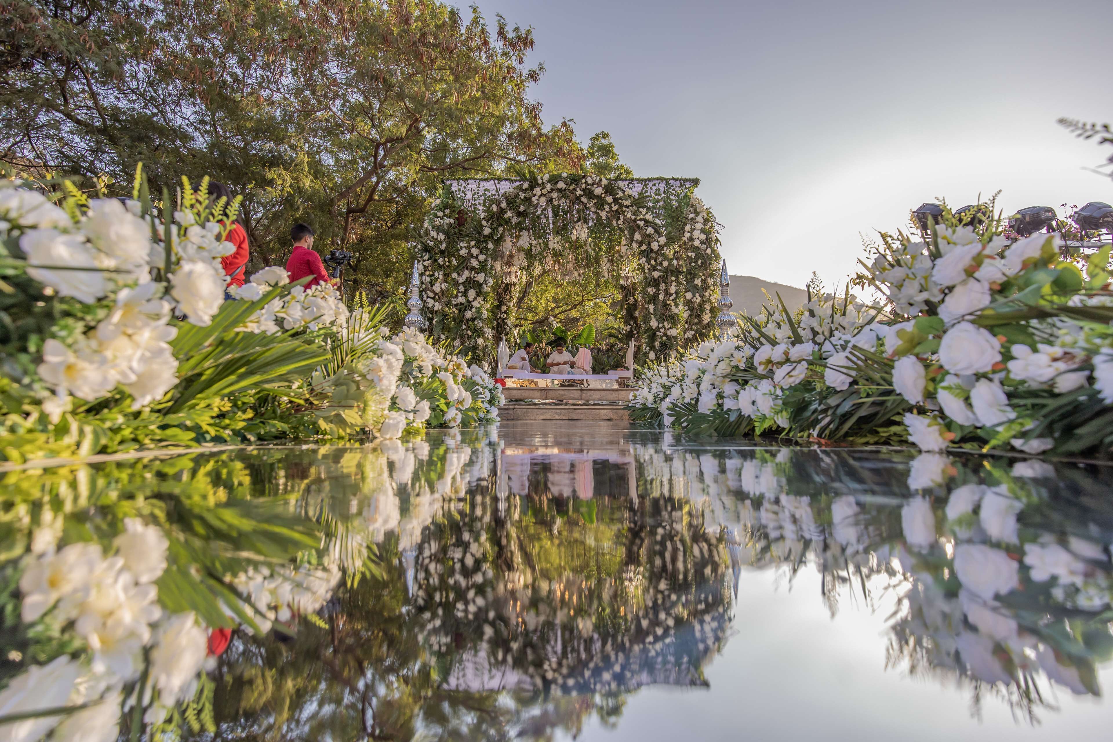 A serene outdoor setting with a reflective water surface, a floral archway, and a seating area.
