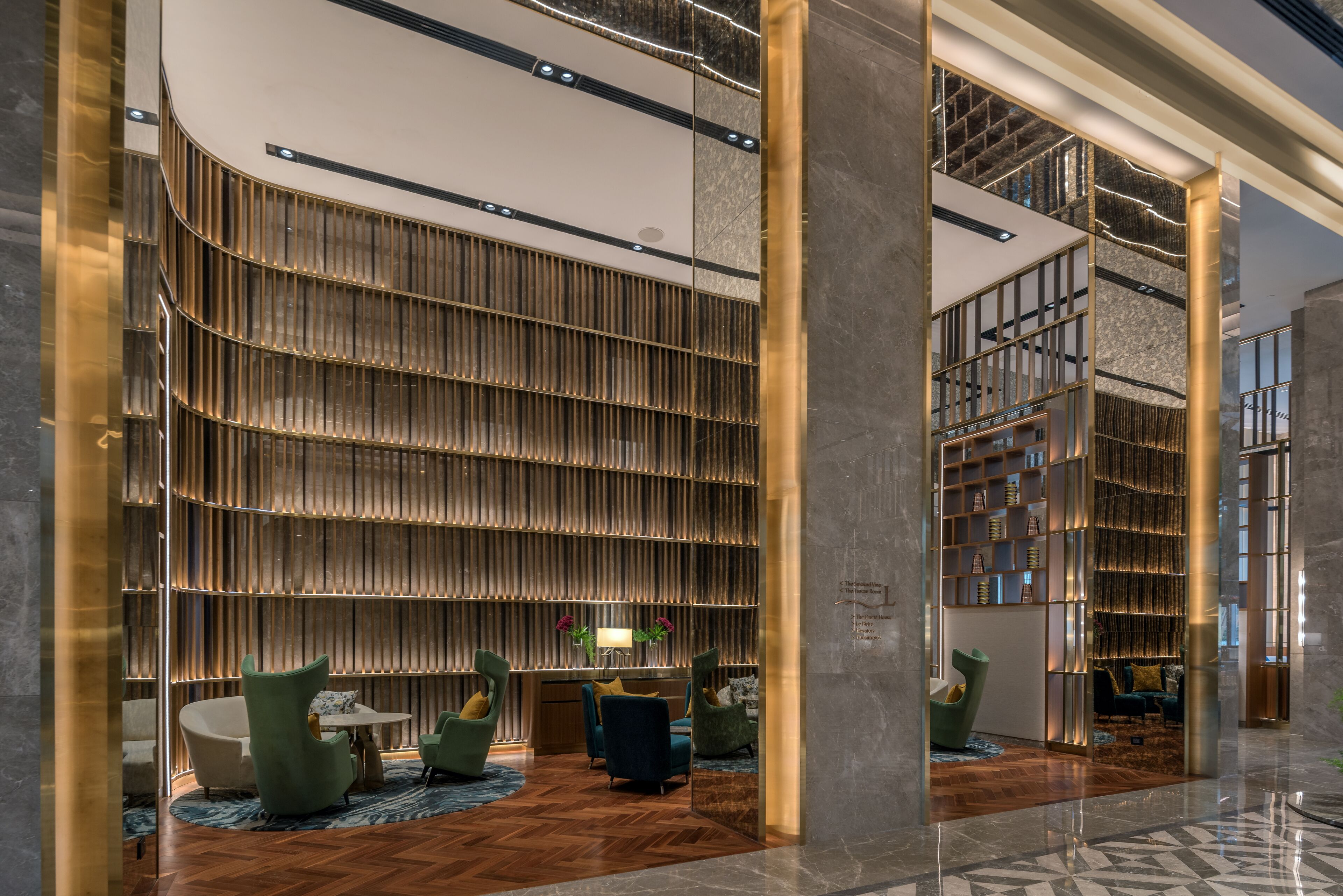 A modern lobby with a curved wall of vertical slats, a reception desk, and seating areas with green chairs and a blue sofa.